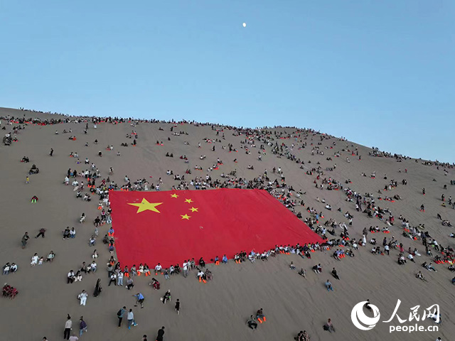 鳴沙山上，各地游客圍坐在巨幅國旗周圍等待萬人星空演唱會開啟。人民網(wǎng) 李根攝