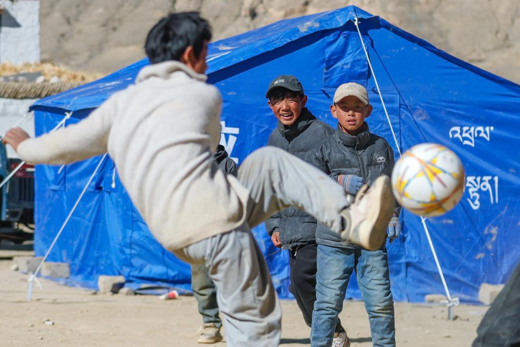 1月11日，在定日縣曲洛鄉(xiāng)措昂村，孩子們在臨時(shí)安置帳篷間的空地上踢足球。（新華社記者 沈伯韓 攝）